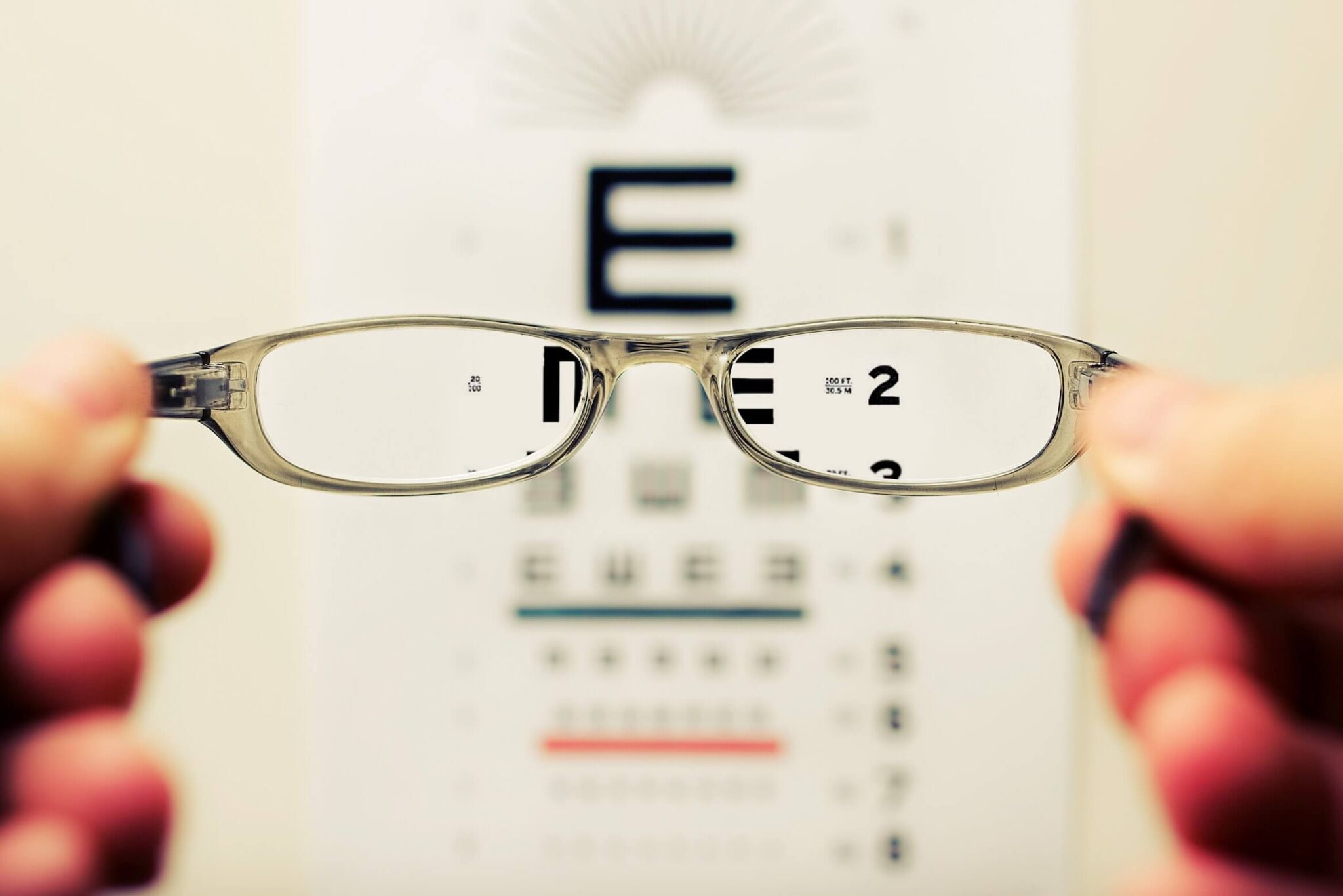 Two hands holding up glasses in front of an eye chart.