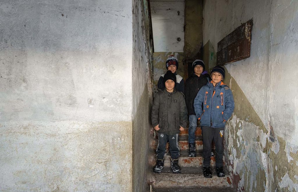Four Kazakh kids standing in an apartment stairwell while wearing winter gear.