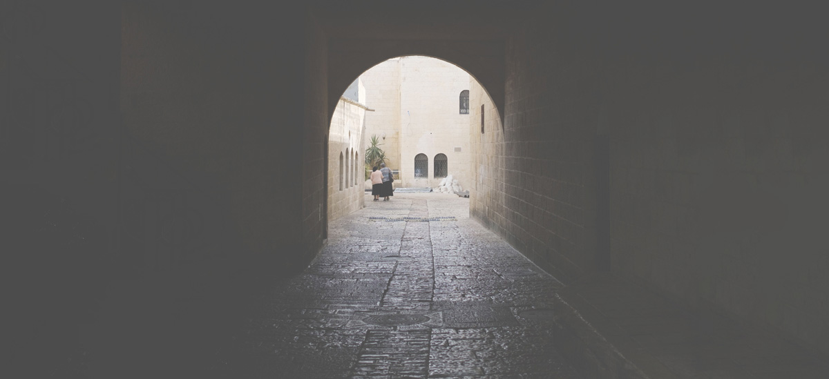 Two women walking through a tunnel on a cobblestone road